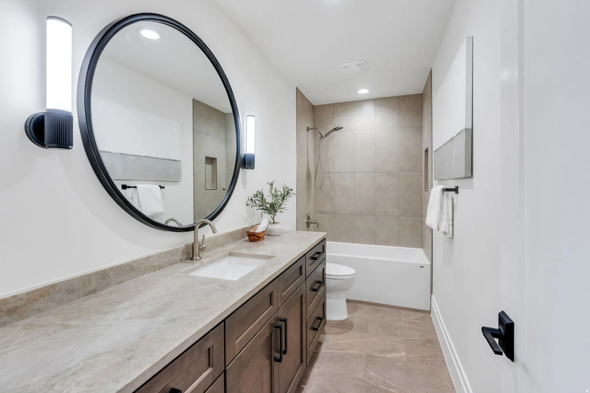 Bathroom featuring a dark wood-finish vanity with a light-toned countertop, a large round mirror, and wall-mounted sconce lighting