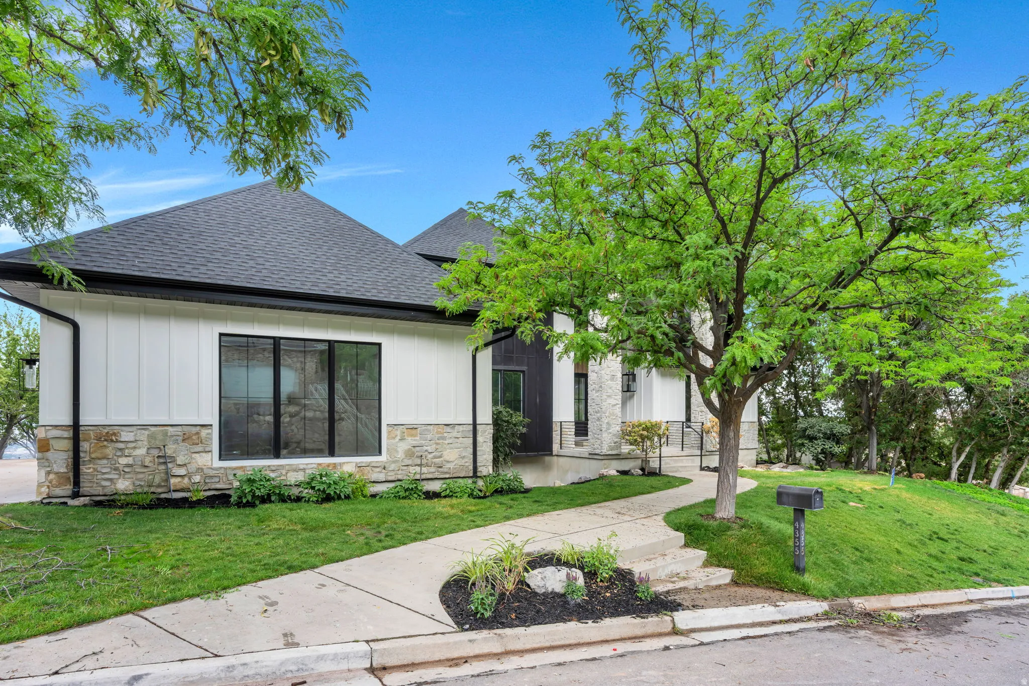 Modern dwelling featuring a dark shingle roof, white vertical siding, and a stone foundation