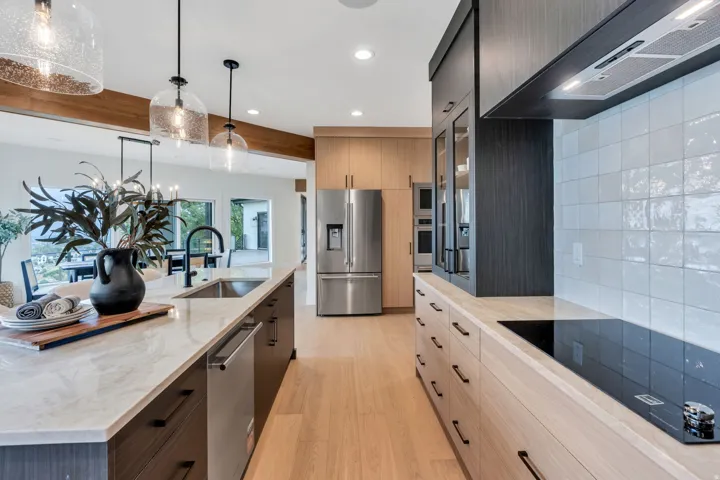Gourmet kitchen featuring a large central island with an undermount sink, stainless steel appliances, wood-finish flooring, light-toned cabinetry, and dark-toned accent cabinetry