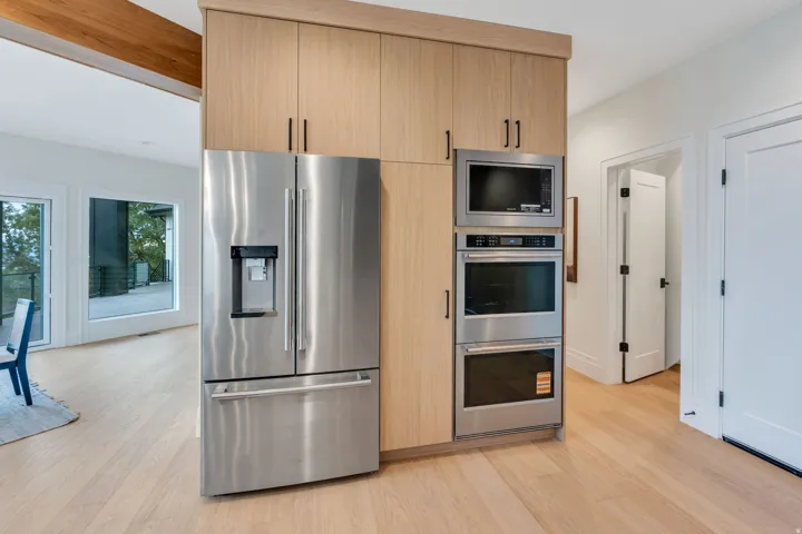 Integrated stainless steel appliances within wood-finish cabinetry, featuring a full-size refrigerator, built-in microwave, and double wall ovens