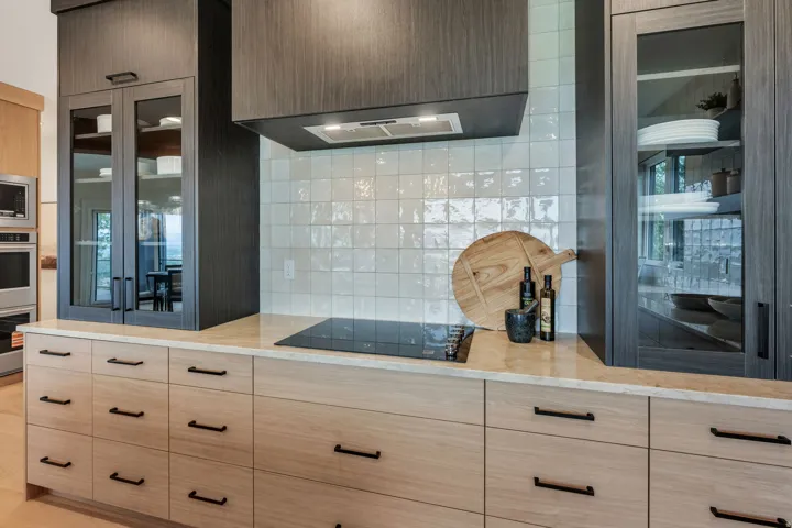 Modern kitchen featuring two-tone cabinetry, a light-toned countertop, a built-in induction cooktop, and a textured white tile backsplash