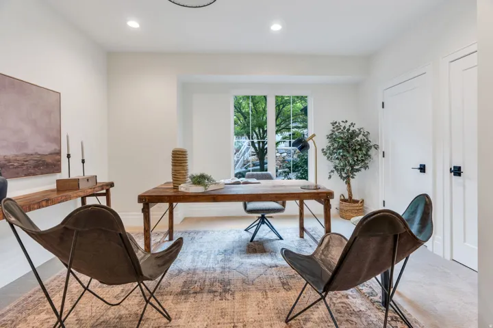 Recessed lighting illuminating a spacious room with a large window, light-toned walls, and twin paneled doors featuring black hardware