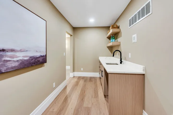 Built-in wet bar featuring a white countertop, undermount sink with a matte black faucet, and wood-finish cabinetry