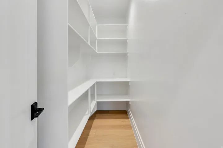 Expansive walk-in pantry featuring white built-in shelving, light wood-finish flooring, and bright overhead lighting