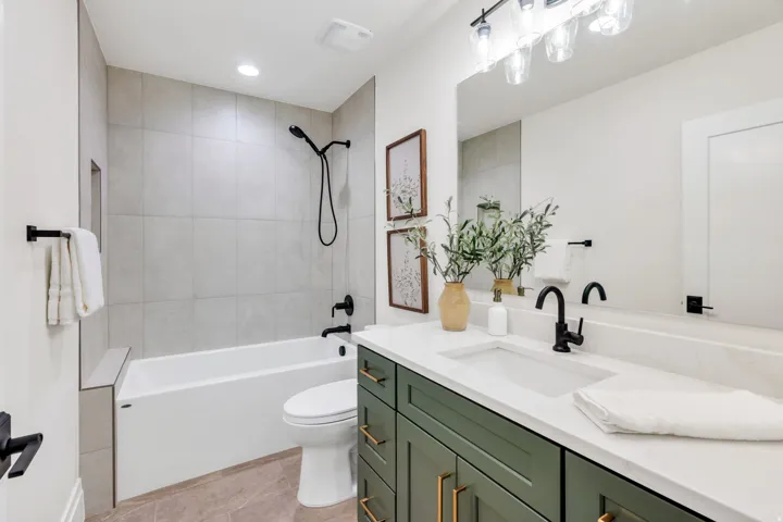 Bathroom featuring a deep green vanity with gold-tone hardware, a white countertop with an integrated sink, and a large wall-mounted mirror