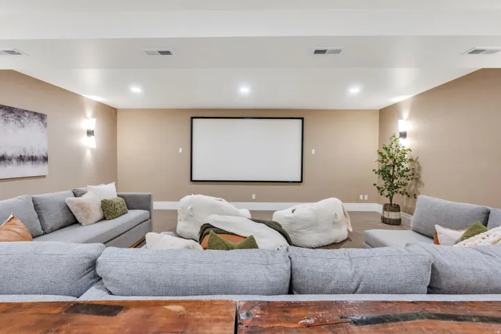 Spacious entertainment room featuring a large projection screen, recessed lighting, wall sconces, and neutral wall tones