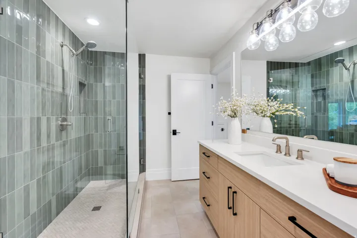 Full-length mirror illuminating a light wood-finish vanity with an integrated rectangular sink and brushed nickel faucet