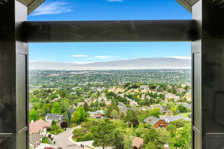 Expansive landscape scenery featuring a distant body of water, mountains, and a verdant residential area