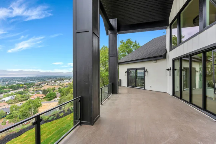 Expansive outdoor terrace featuring dark-framed glass railings, large format sliding glass doors, a smooth concrete surface, and substantial structural columns