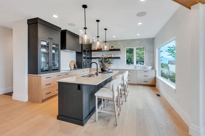 Modern kitchen featuring a large central island with seating, light wood-finish flooring, dark and light wood-finish cabinetry, light stone countertops, and multiple windows