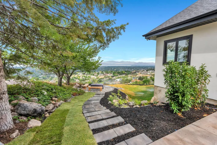 Terraced landscaping featuring a stone paver pathway, mature trees, manicured lawn, and planted garden beds