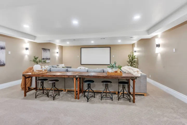 Spacious room featuring a large projection screen, recessed lighting, wall sconces, and neutral-toned carpeting
