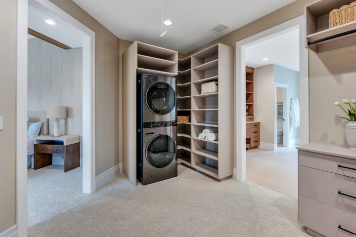 Laundry area featuring a stacked washer and dryer, integrated shelving, and light-toned carpeting