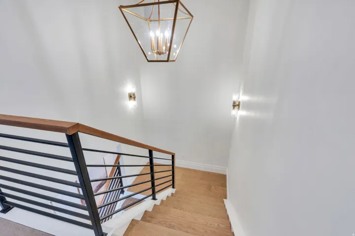 Modern staircase featuring wood-finish treads, a contemporary black metal and wood-finish railing, and a geometric brass light fixture