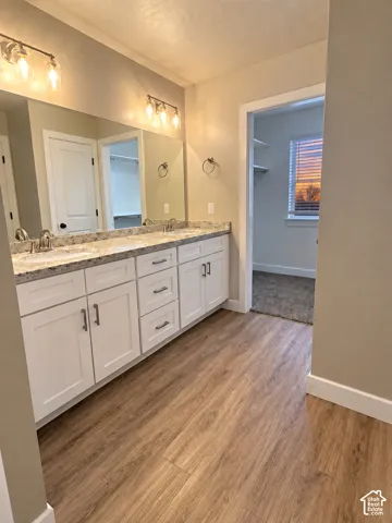 Dual vanity with a speckled countertop, white cabinetry, and wood-finish flooring