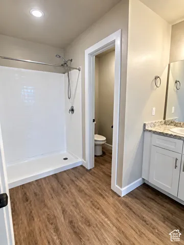 Walk-in shower with white tile surround, wood-finish flooring, white vanity with stone countertop, and recessed lighting