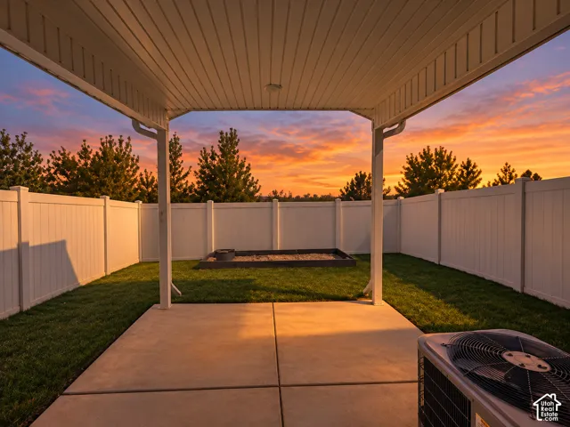 Covered patio with concrete flooring, surrounded by a white privacy fence and a manicured lawn