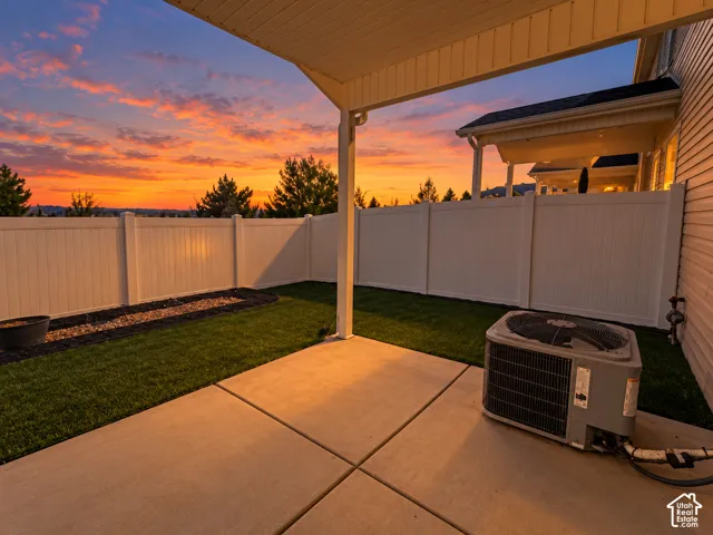 Covered patio with concrete paving, turf lawn, and white privacy fencing