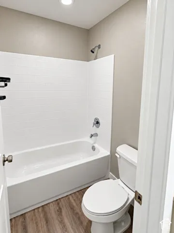 Bathtub-shower combination with white subway tile surround, chrome fixtures, recessed lighting, and wood-finish flooring