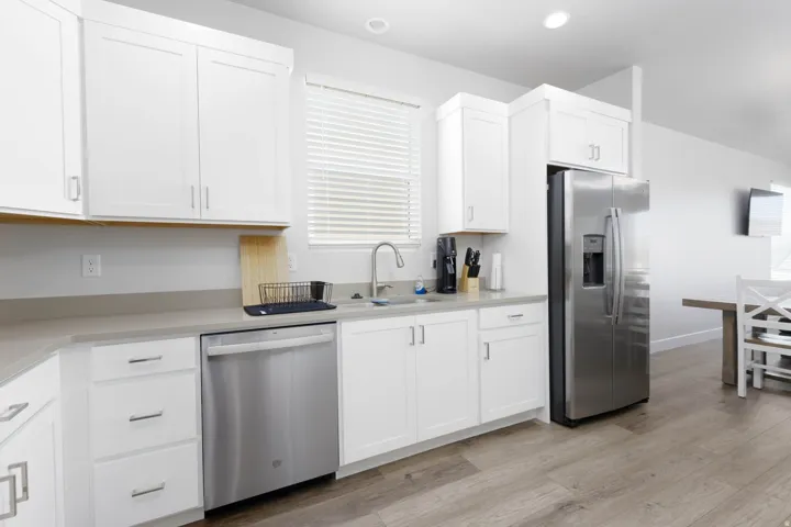 Kitchen featuring white shaker cabinetry, stainless steel appliances, light-toned countertops, and wood-finish flooring