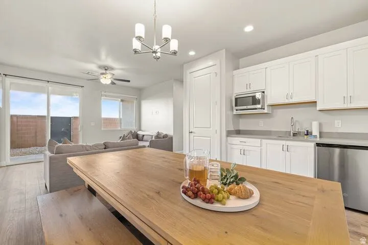 Open-concept living space featuring wood-finish flooring, a contemporary chandelier, a ceiling fan, and a kitchen area with white cabinetry, stainless steel appliances, and a built-in microwave