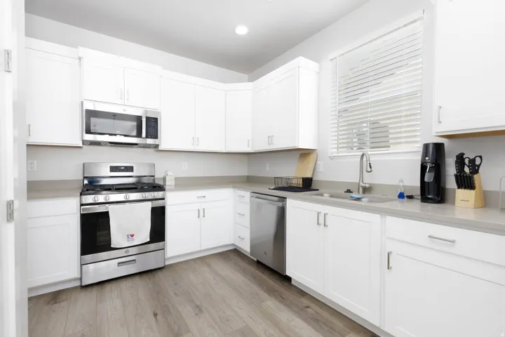 Modern kitchen featuring white shaker cabinetry, stainless steel appliances, light gray countertops, a stainless steel sink with a gooseneck faucet, and wood-finish flooring