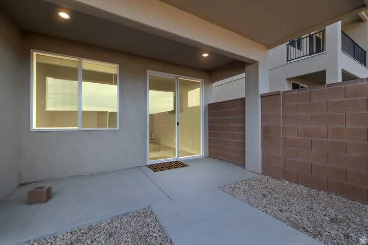 Covered patio featuring concrete flooring, recessed lighting, block wall fencing, sliding glass door, and a window with white framing