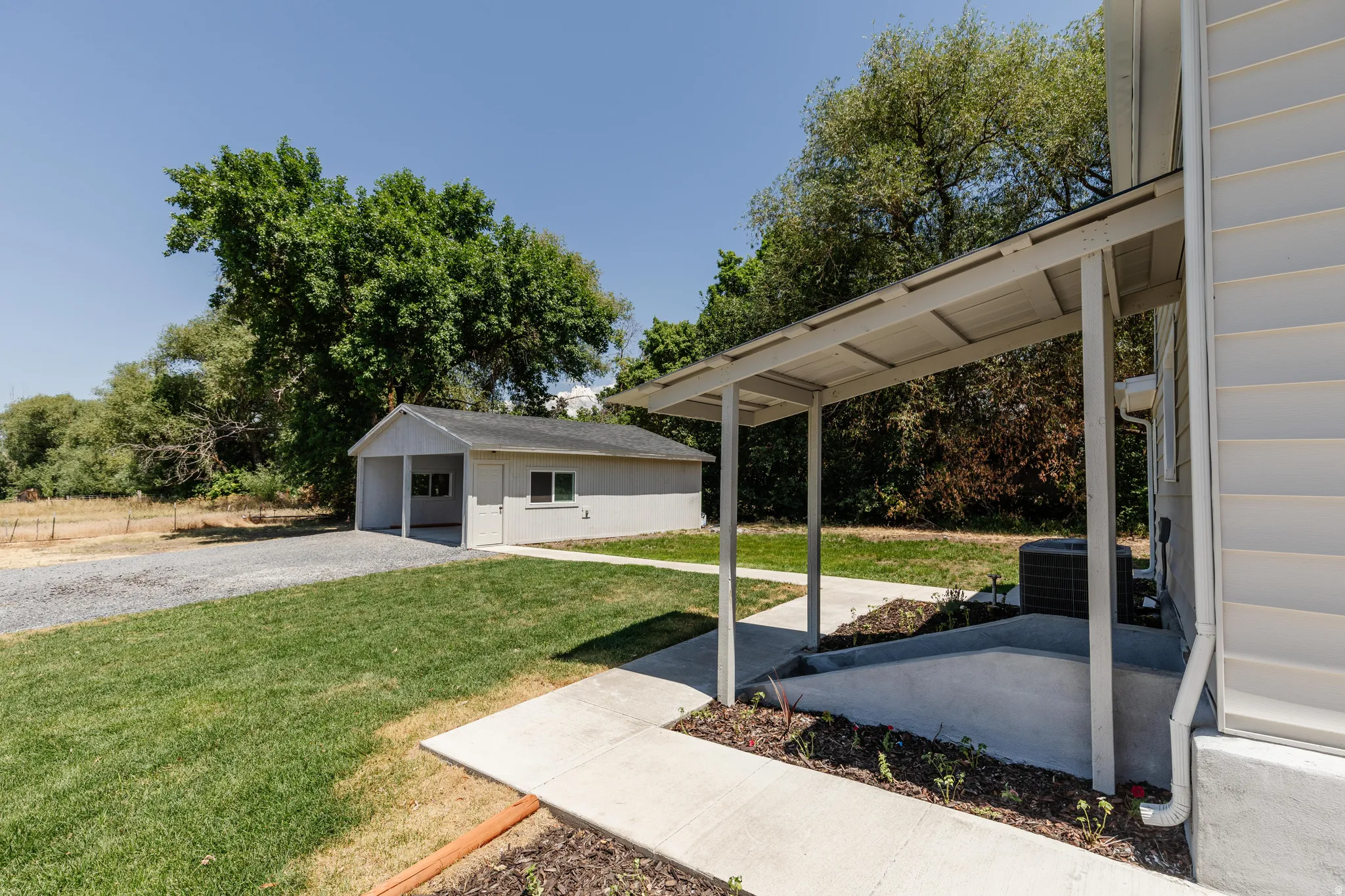 Detached garage structure with a covered carport, gravel driveway, and surrounding green lawn