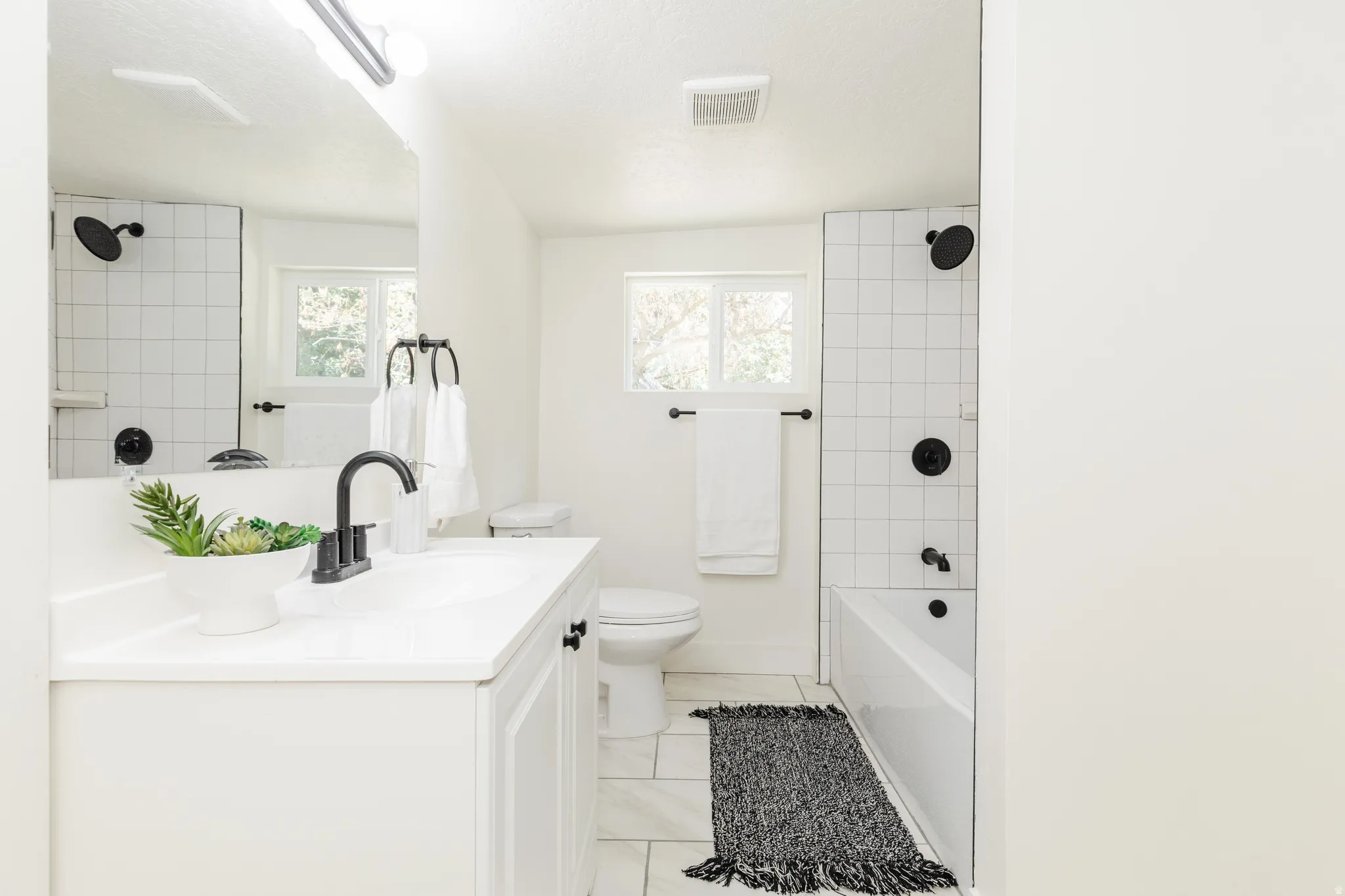 Modern white bathroom featuring a vanity with integrated sink, matte black fixtures, subway tile shower surround, and a window for natural light