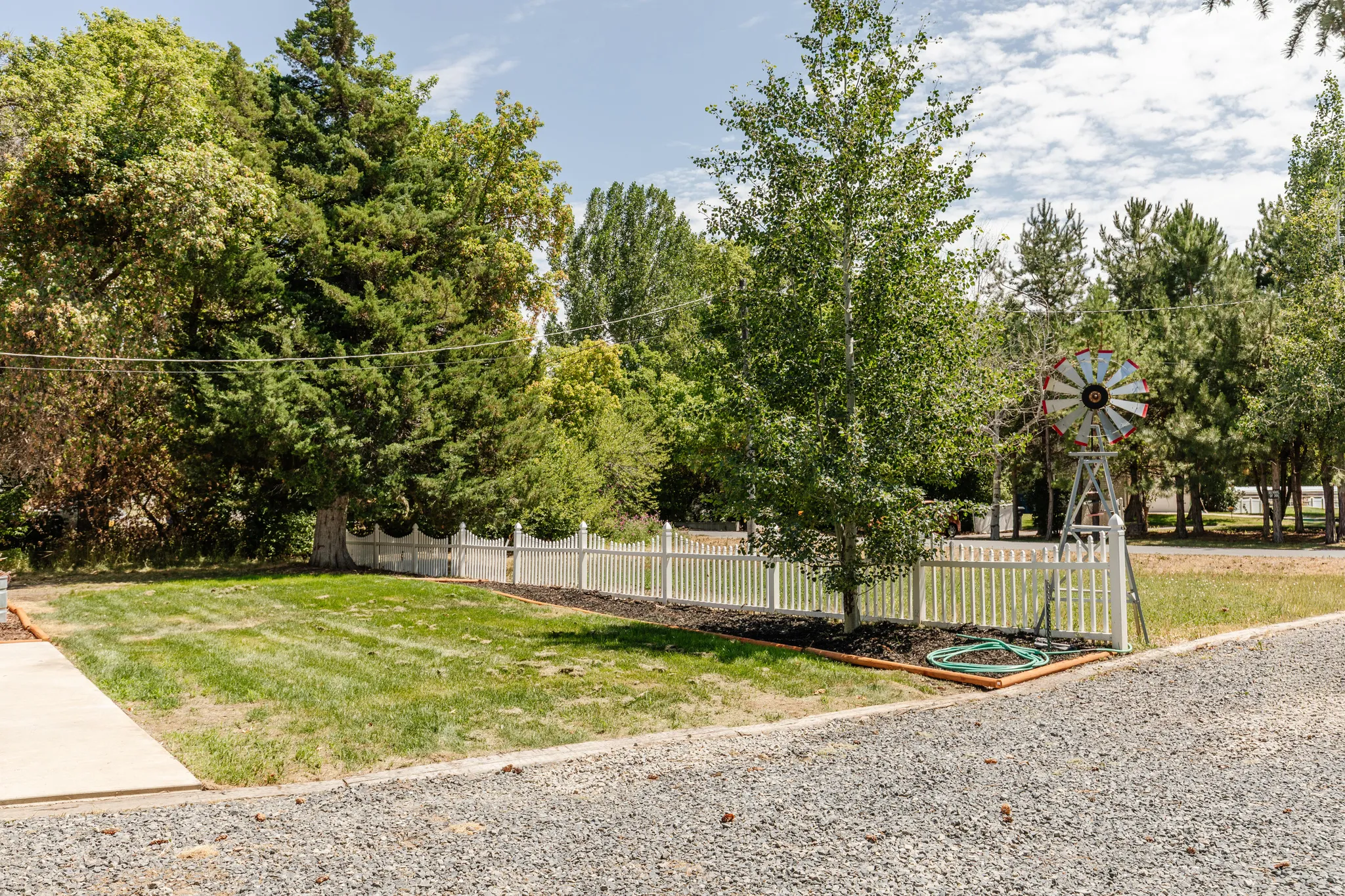 Manicured lawn framed by a white picket fence, mature trees, and a decorative windmill