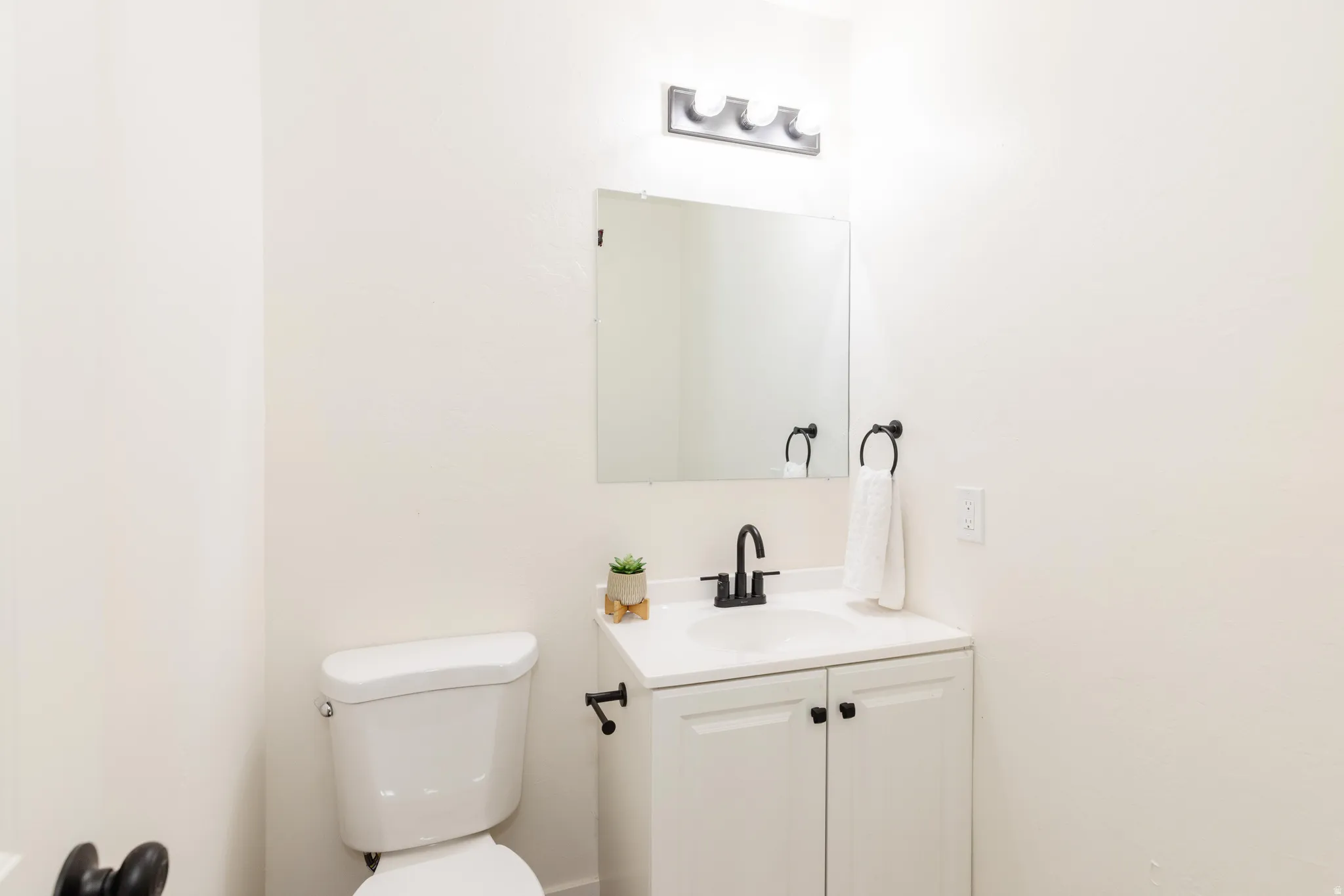 Bathroom featuring a white toilet, single vanity with a black faucet, white cabinetry with black hardware, and an overhead light fixture