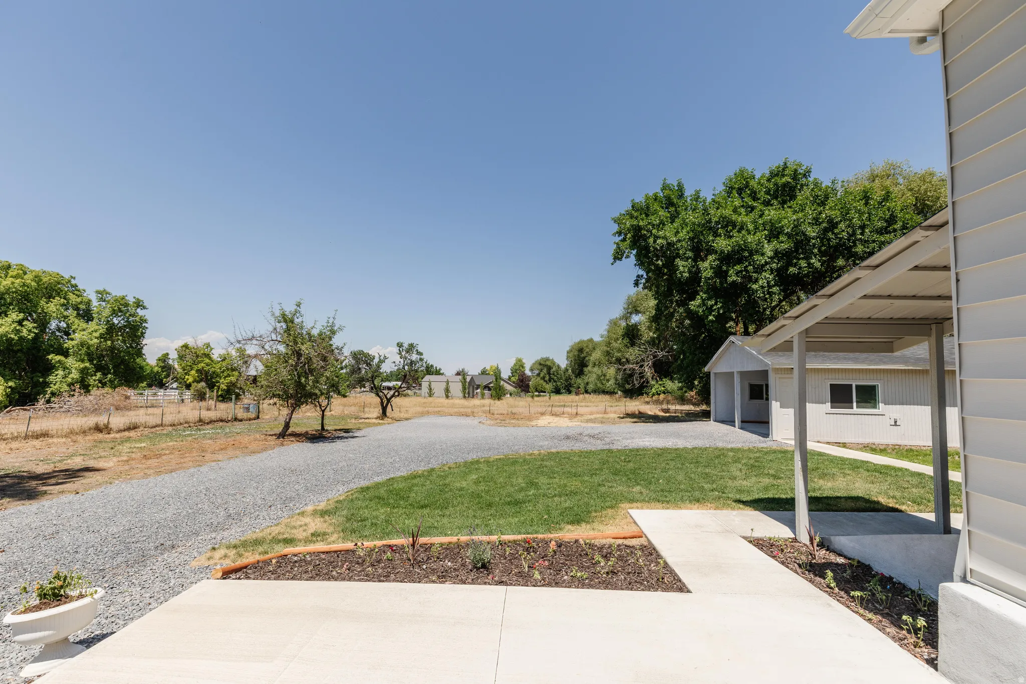 Expansive outdoor area featuring a gravel driveway, mature trees, and a detached structure with a covered entry