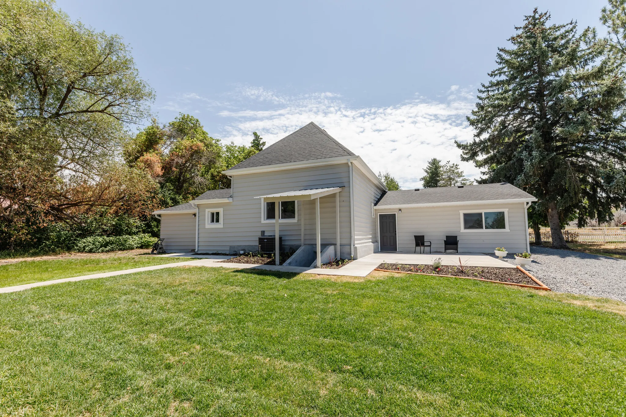 Expansive grass lawn with concrete walkways leading to a covered entryway and patio