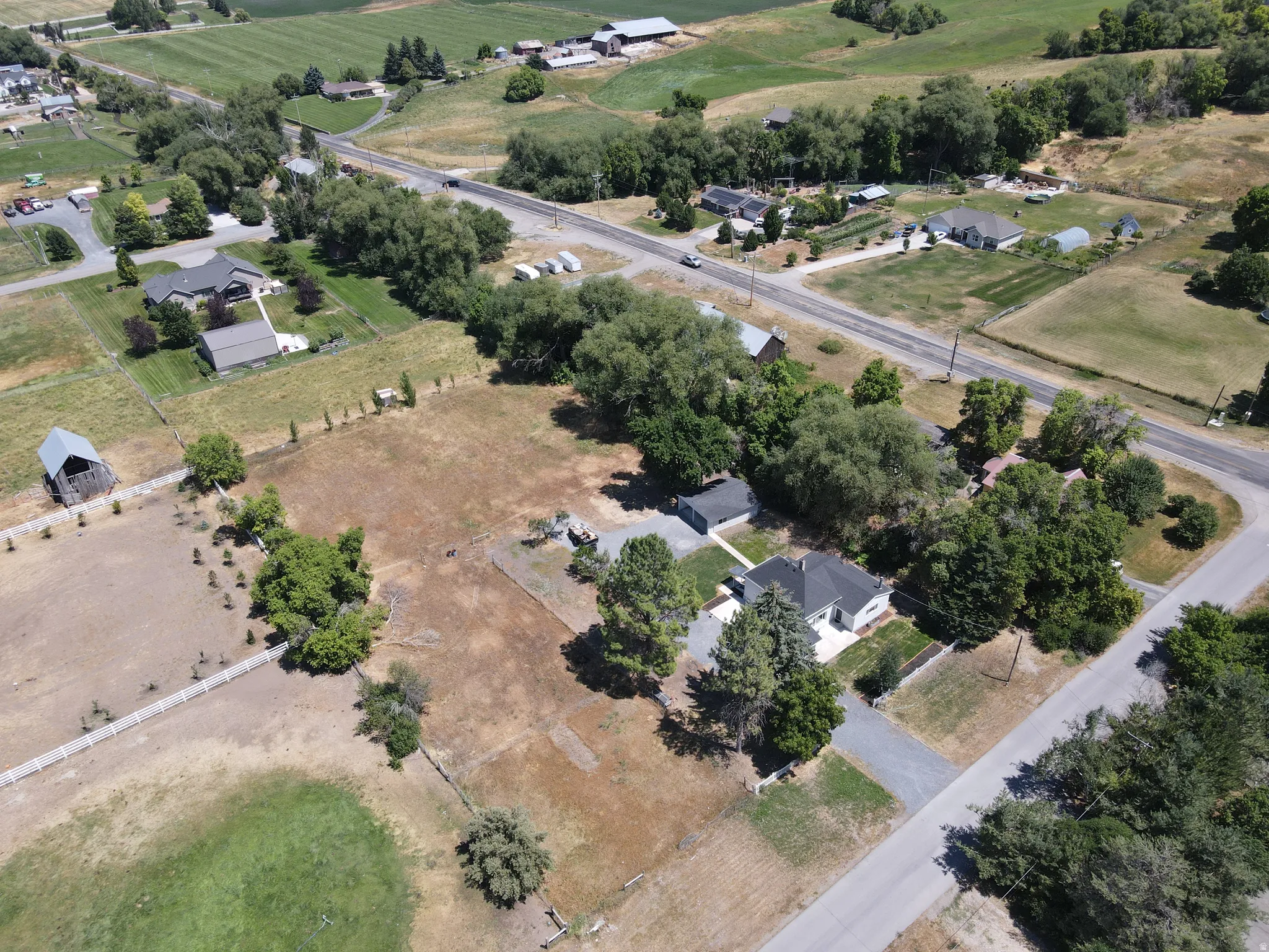 Aerial view showcasing a residential property with a dark-roofed home, surrounded by mature trees and a gravel driveway