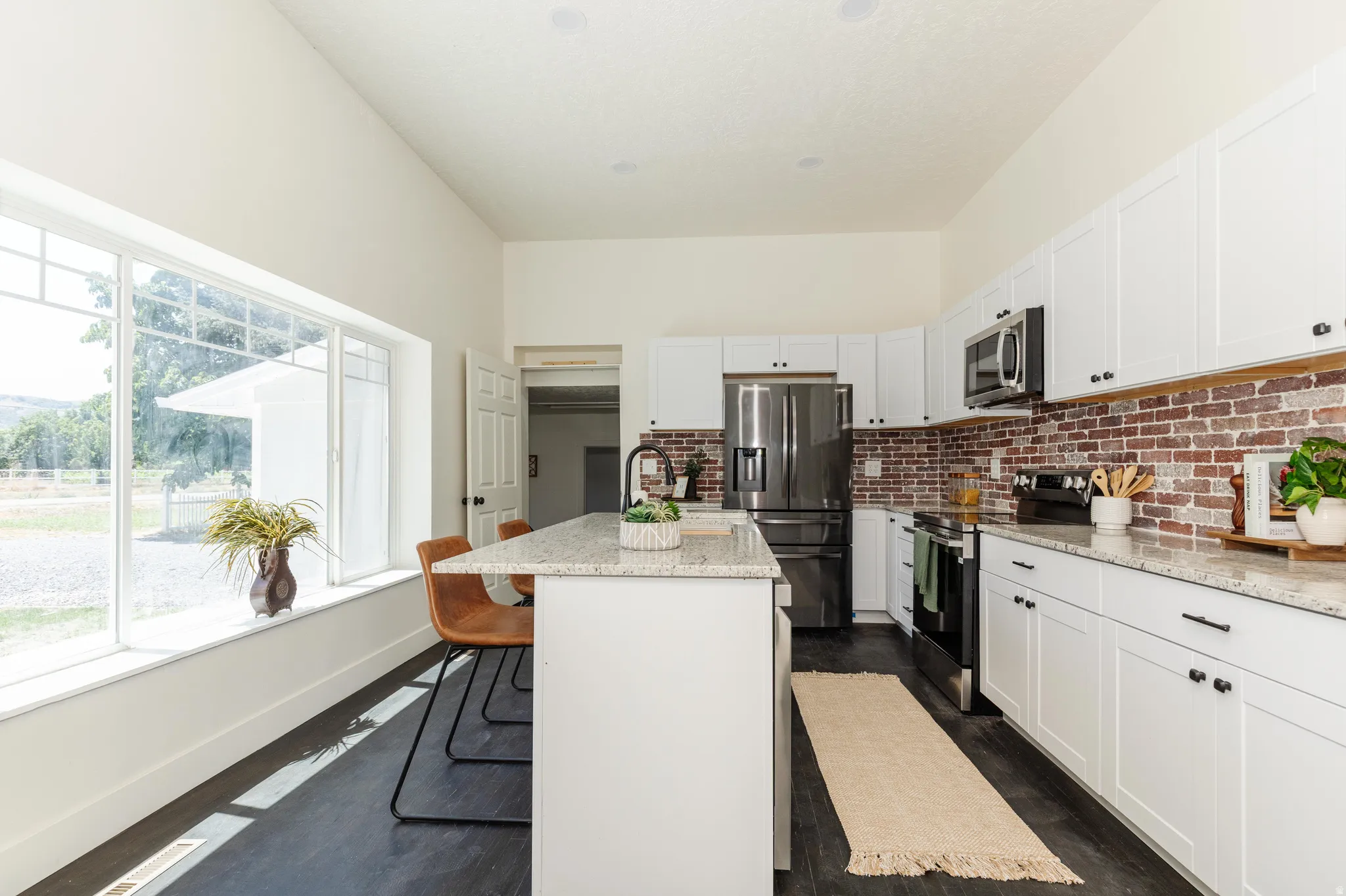 White kitchen featuring a large window, granite countertops, stainless steel appliances, brick-finish backsplash, and dark wood-finish flooring