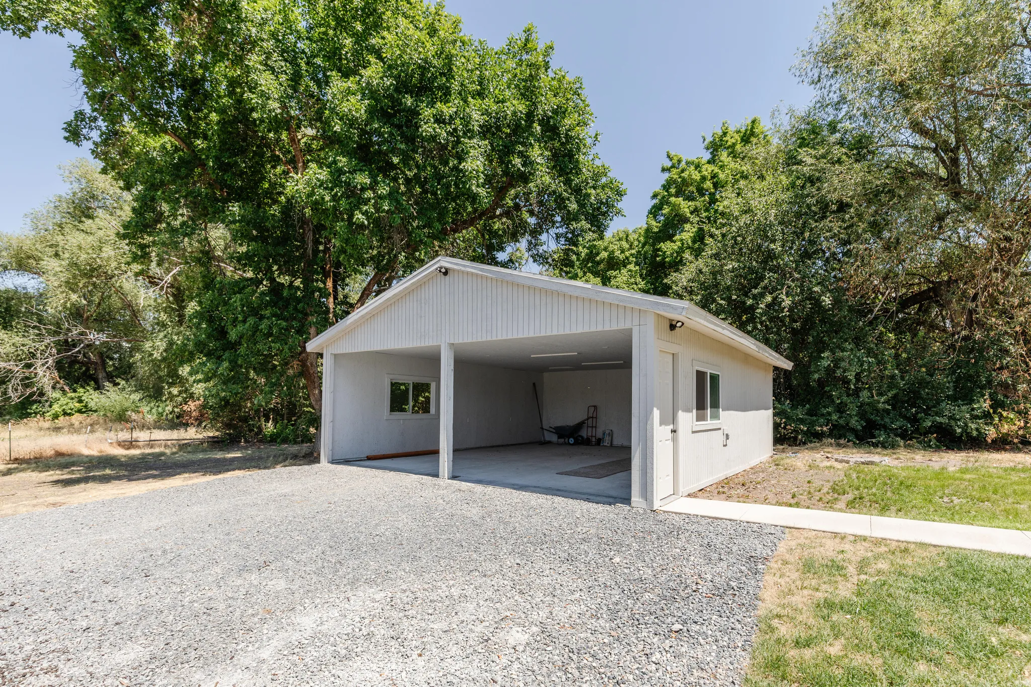 Detached carport structure featuring a light-colored exterior, two open bays, and a side access door