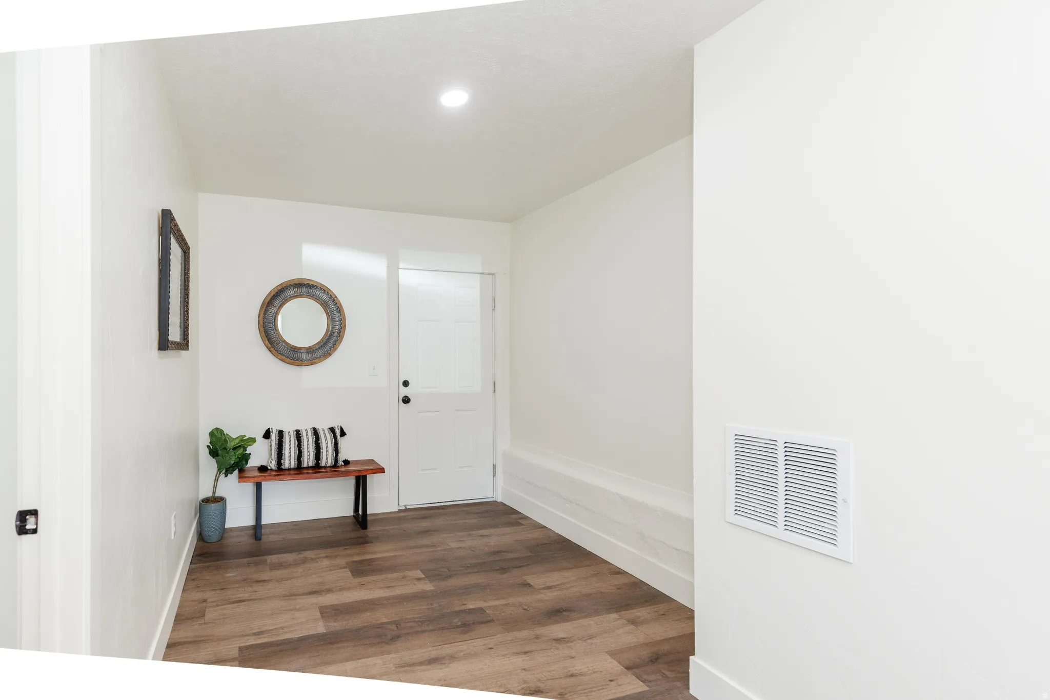 Entryway featuring wood-finish flooring, white walls, a white paneled door, recessed lighting, and a built-in wall bench