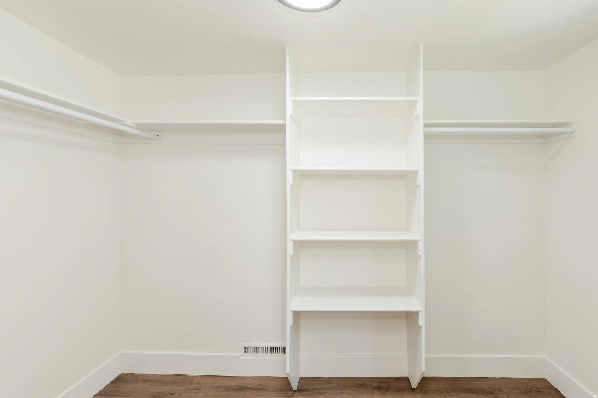Walk-in closet featuring built-in shelving, dual hanging rods, wood-finish flooring, and a flush-mount ceiling light