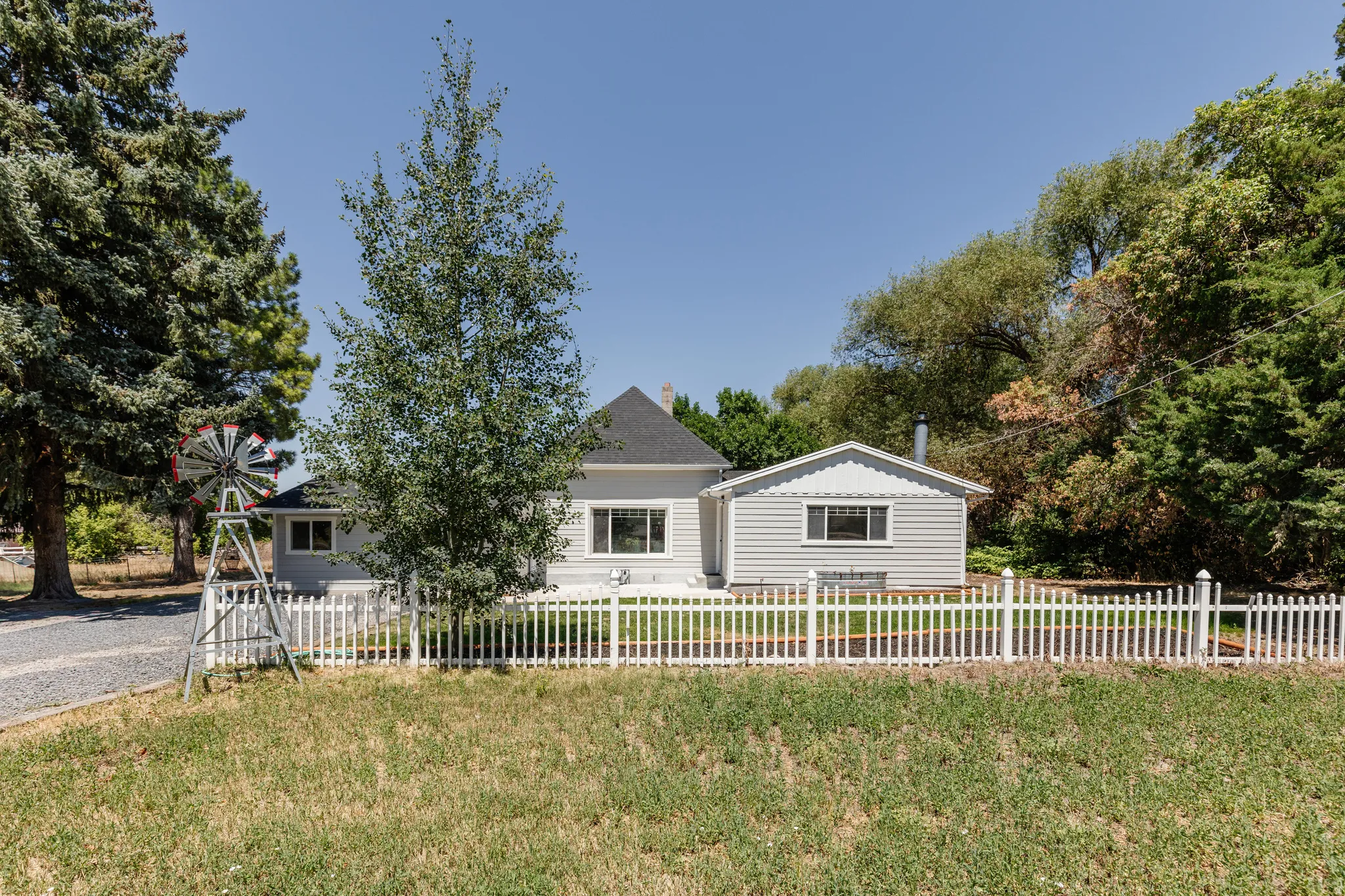 Light gray exterior siding with white trim, a white picket fence, and mature trees