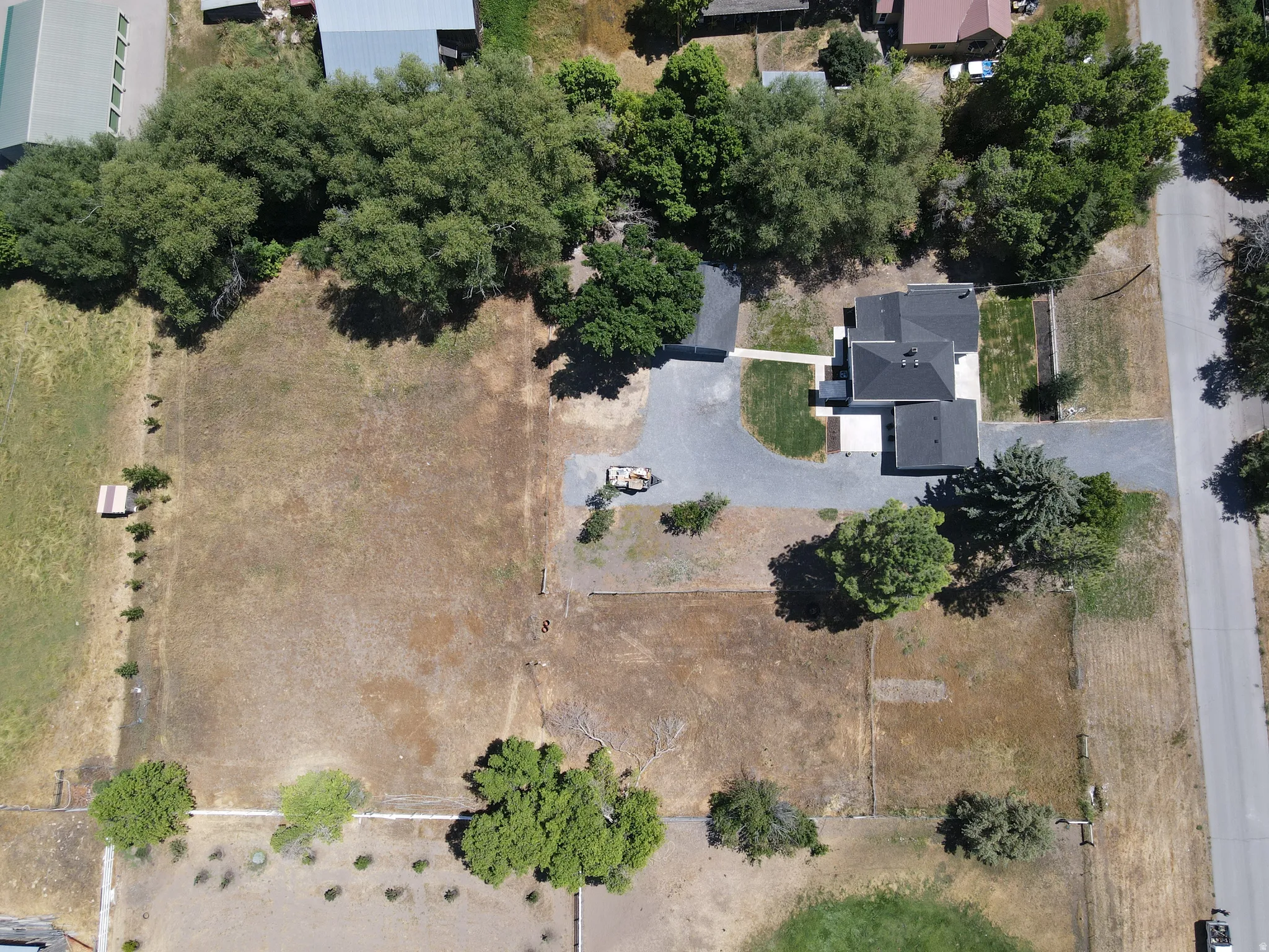 Aerial perspective highlighting the property's expansive land, featuring a single-story residence with a dark roof, a gravel driveway, and surrounding mature trees