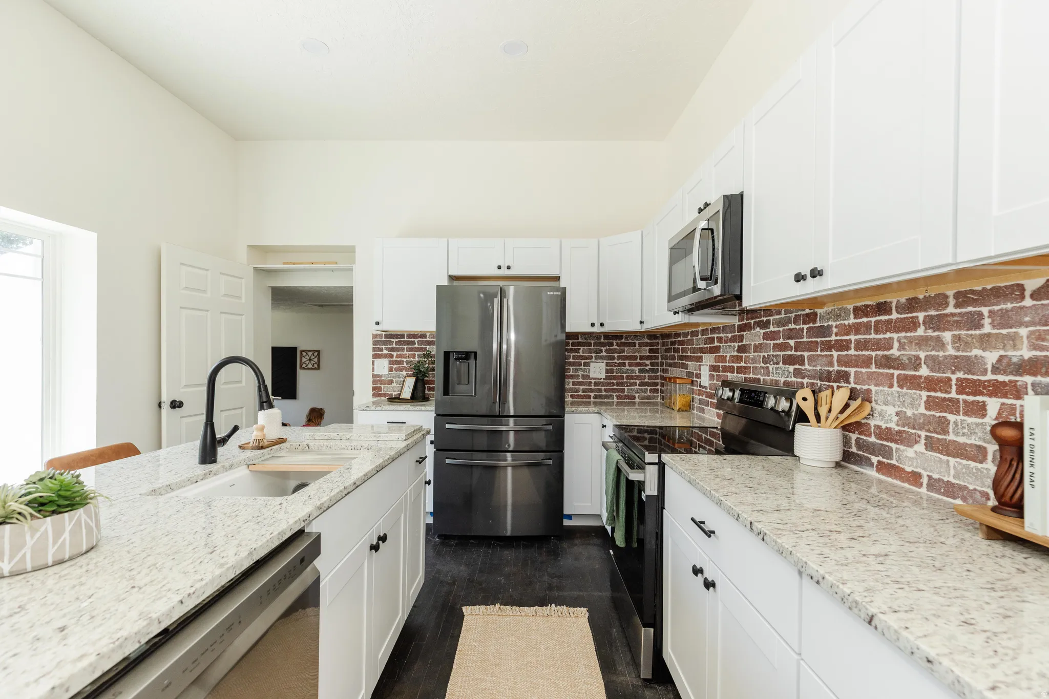 Kitchen featuring white shaker cabinetry, light speckled countertops, a dark brick backsplash, and dark wood-finish flooring
