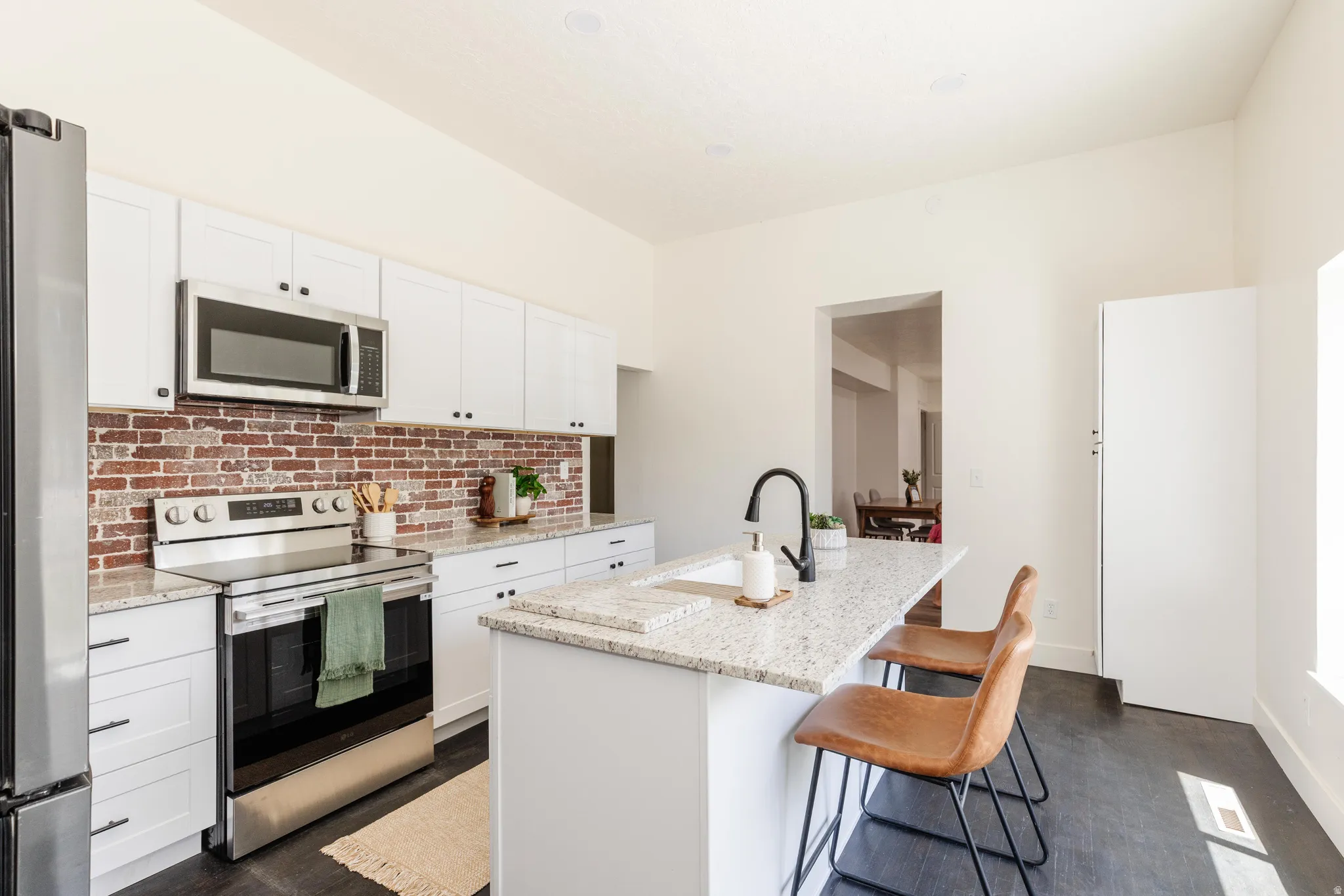 Kitchen featuring a large central island with seating, white shaker-style cabinetry, granite countertops, and a brick-patterned backsplash