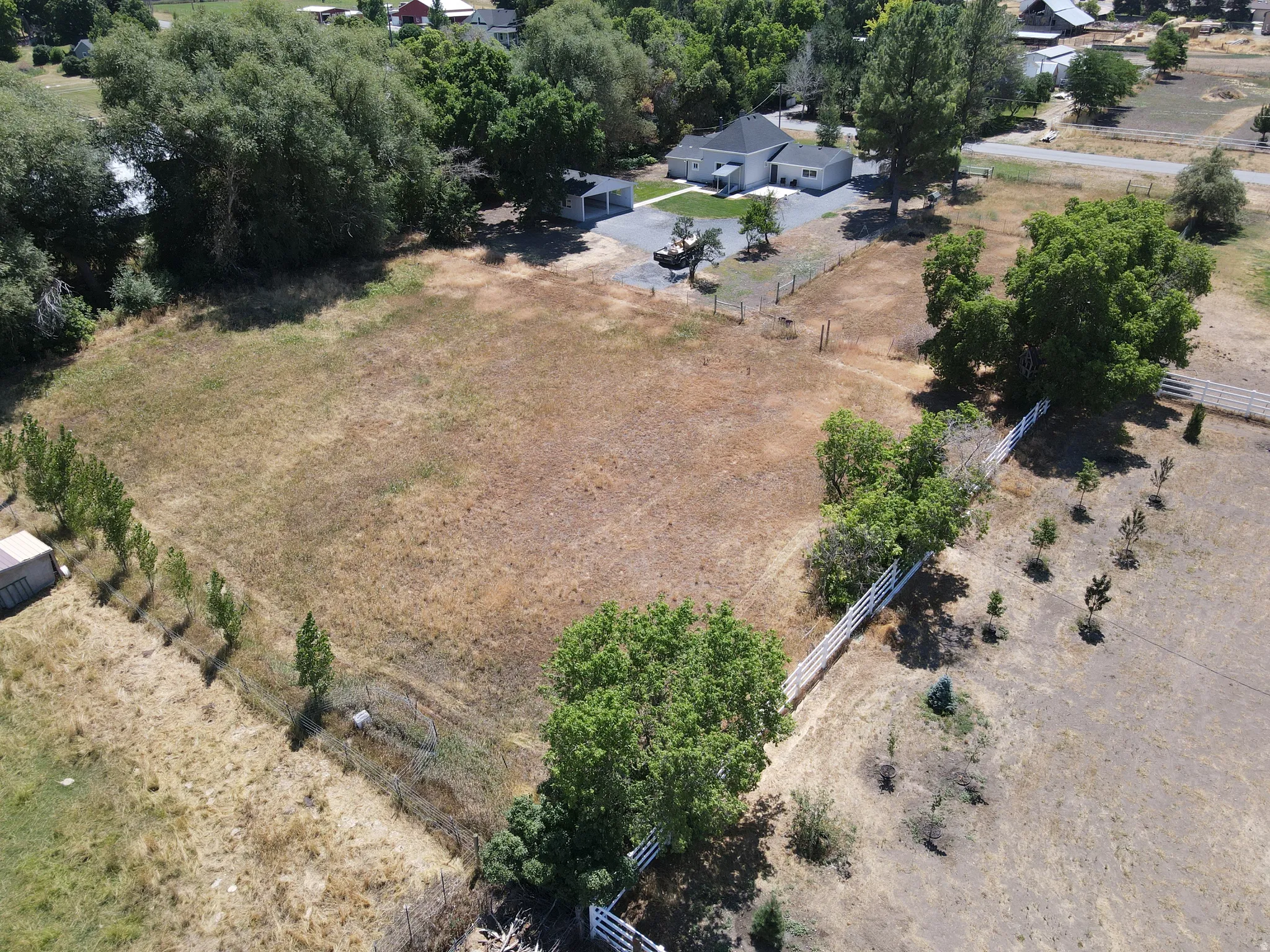 Expansive lot with a single-story residence and detached garage, featuring mature perimeter trees, a white picket fence, and additional smaller trees