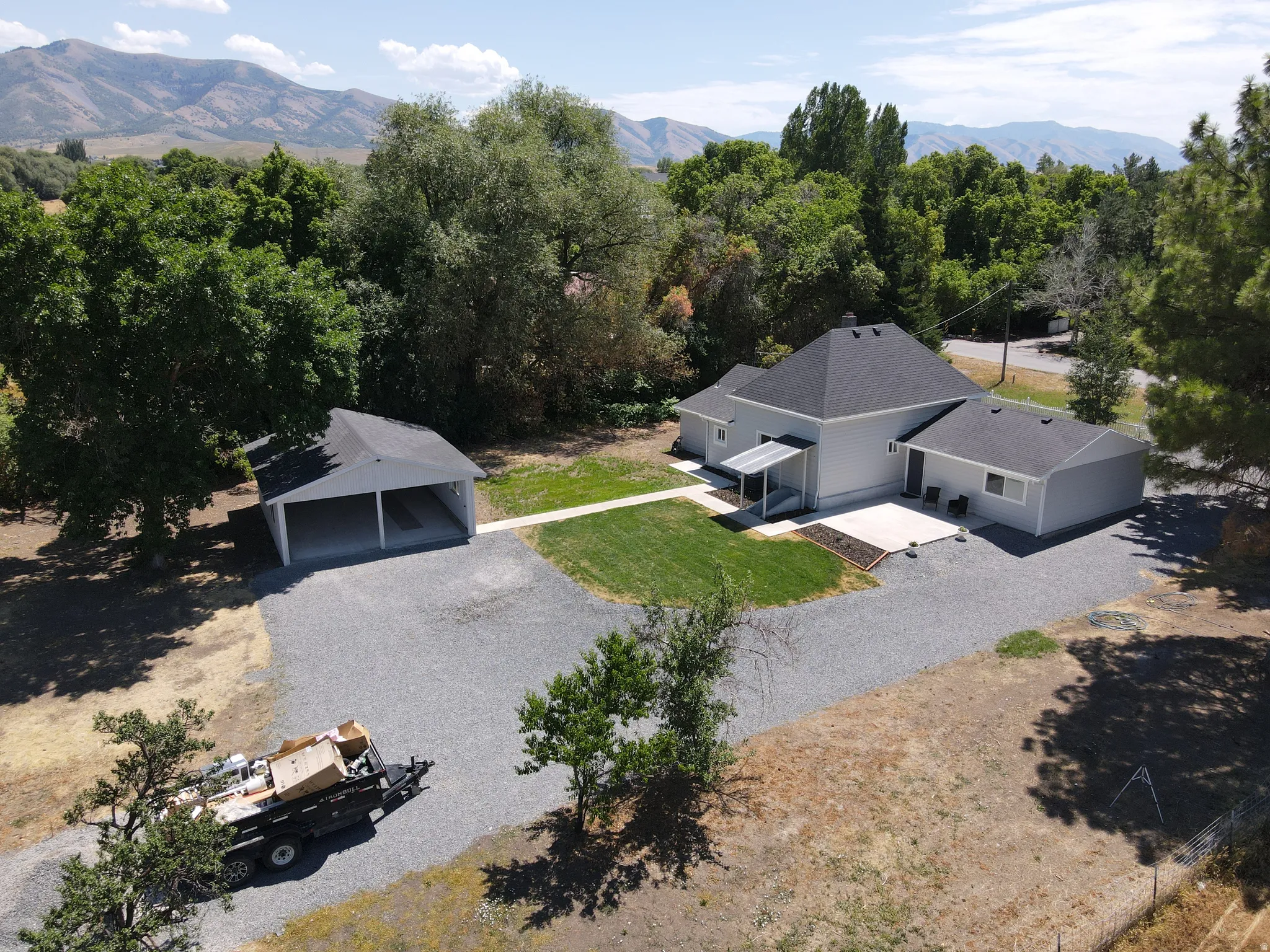 Expansive gravel driveway leading to a two-car carport and a light gray residence with a dark shingle roof