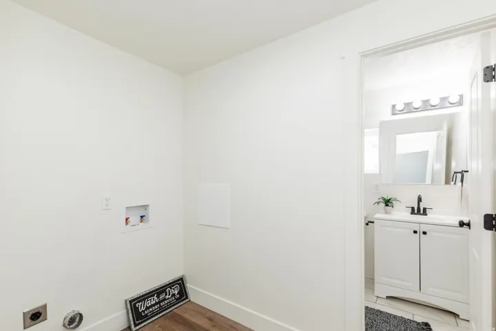 Dedicated laundry area with hookups and wood-finish flooring, opening to a bathroom featuring a white vanity with a rectangular sink, black faucet, and a wall-mounted mirror