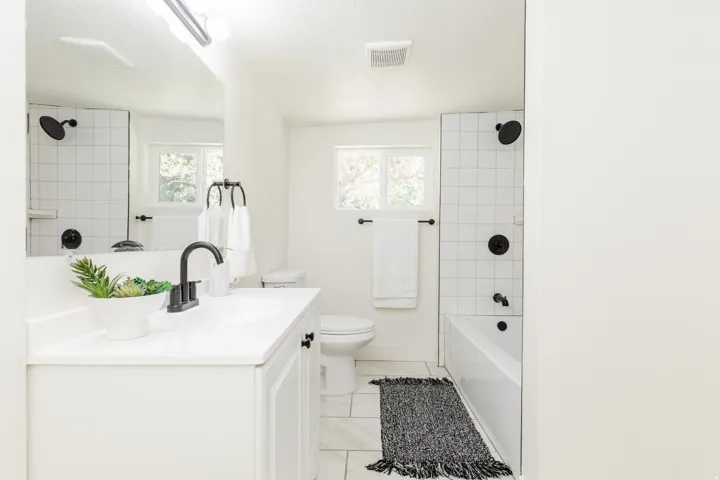 Modern white bathroom featuring a vanity with integrated sink, matte black fixtures, subway tile shower surround, and a window for natural light