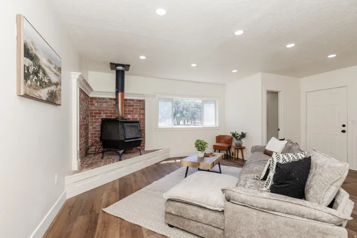 Living area featuring a brick hearth with a black wood-burning stove, recessed ceiling lighting, wood-finish flooring, and a window with exterior views