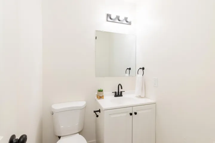 Bathroom featuring a white toilet, single vanity with a black faucet, white cabinetry with black hardware, and an overhead light fixture