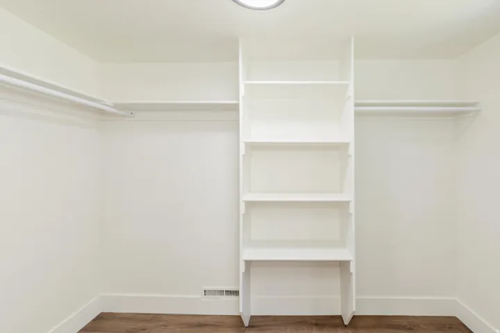 Walk-in closet featuring built-in shelving, dual hanging rods, wood-finish flooring, and a flush-mount ceiling light