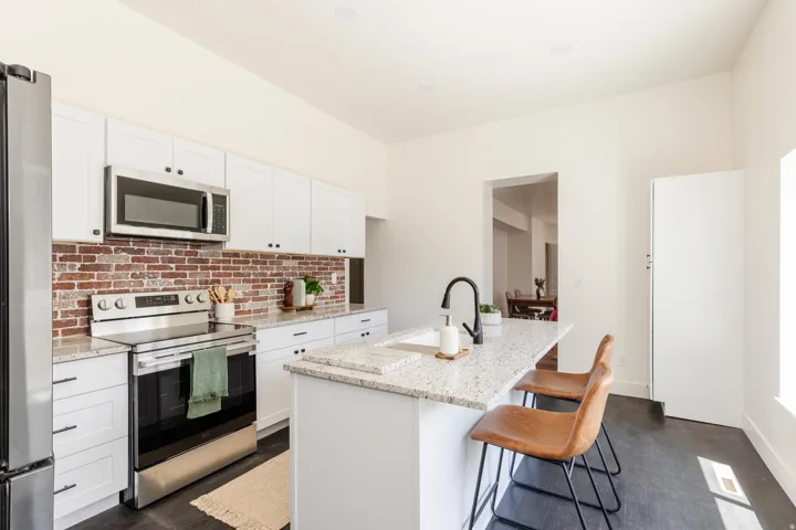 Kitchen featuring a large central island with seating, white shaker-style cabinetry, granite countertops, and a brick-patterned backsplash